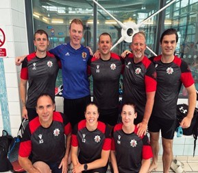 GMFRS swimming team posing pool side. There are eight members of the team and they are all wearing t-shirt and shorts.