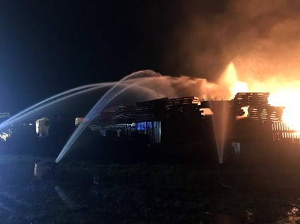 An image in the dark of a building on fire with 3 firefighter hoses spraying at the building