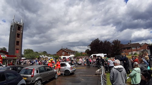 People arriving at Hindley open day, includes training tower, cars, firefighters in uniform and several members of the public.