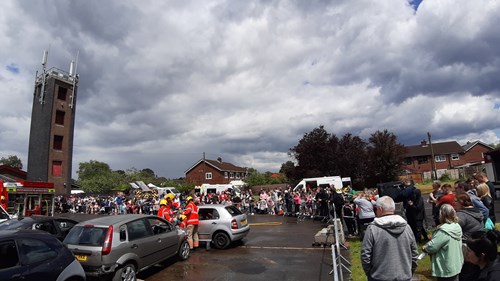 Image shows shot capturing people and activities at Hindley open day - taken out doors and includes training tower, cars, firefighters in uniform and several members of the public
