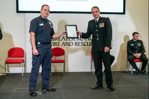 A firefighter and the Chief Fire Officer stand on a stage during a presentation ceremony