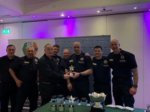 The Greater Manchester team is presented with their trophy. They stand in a line holding the award and smiling at the camera