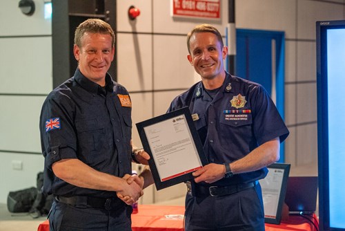 Chief Fire Officer Dave Russel presents David Hedgecock with a certificate. Both look into the camera and smile