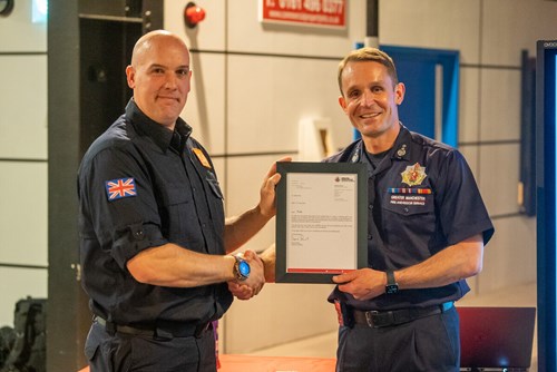 Chief Fire Officer Dave Russel presents Mike Hirst with a certificate. Both look into the camera and smile