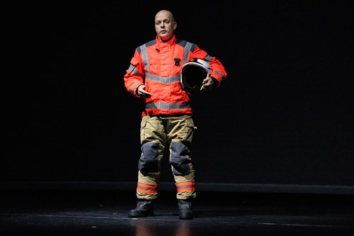 Firefighter in uniform holding a helmet on a stage.