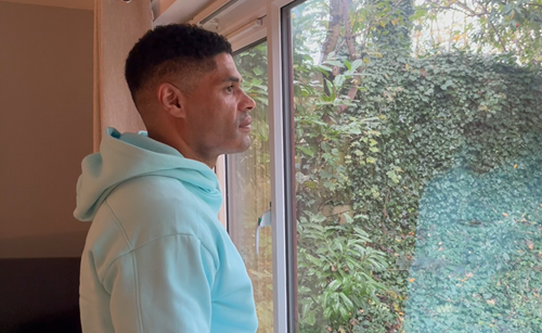A person wearing in a hoodie looking out of a window.