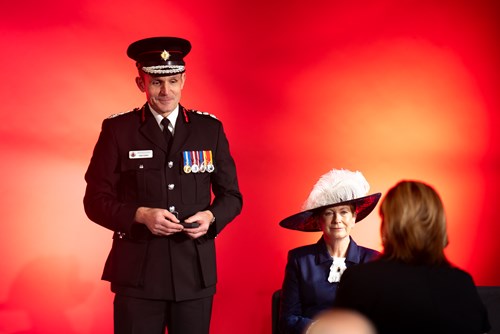 Chief Fire Officer, Dave Russel holding a 30-year clasp box while on stage, smiling at a recipient who is entering the frame ready to receive their award.