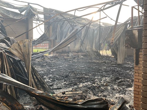 An interior view of a fire-damaged building, with burnt metal and ashes on the ground