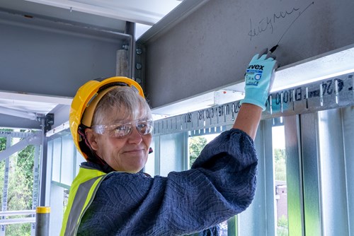 A person smiling wearing high visibility jacket and a hard helmet whilst signing a steel beam