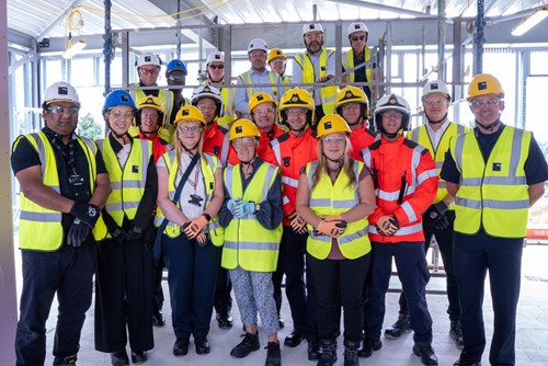 A group of 20 people wearing high visibility jackets, hard helmets and gloves on a construction site