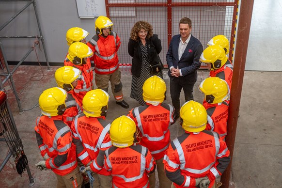 Two people speaking to a group of firefighters.